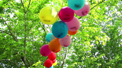 Colorful balloons tied in garland wobble or flutter depending the wind on the green summer foliage background - Powered by Adobe