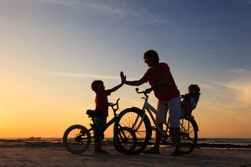 Obraz na płótnie Canvas Biker family silhouette, father with two kids on bikes