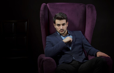 Fototapeta na wymiar Handsome man sitting in the armchair, dark background