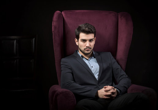 Handsome man sitting in the armchair, dark background