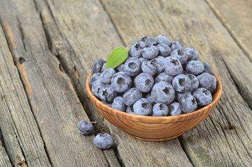 Freshly picked juicy blueberries with green leaves in wooden bowl on rustic table. Blueberry antioxidant. Concept for healthy eating and nutrition.