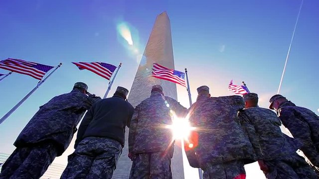 American soldiers saluting the American Flag at the Washington monument with blue sky and lens flare, patriotic.  Handheld.