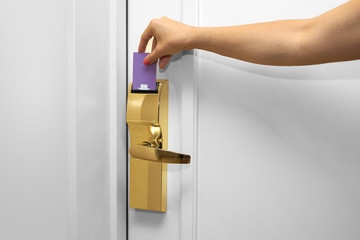 Young woman holding a keycard in front of the electronic sensor of a room door