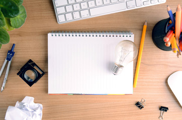 Top view of office desk with paper, stationery, computer, flower, blank notepad and light bulb. Concept for graphic design, marketing, big idea, creative workflow, project management.