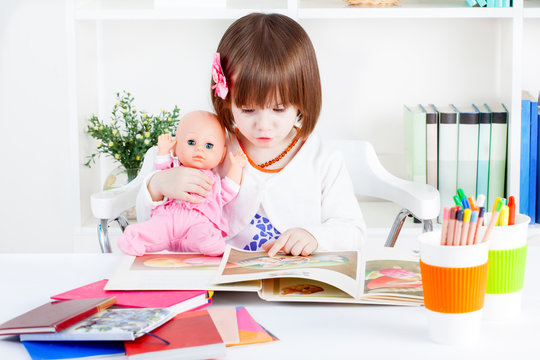 Cute little girl reads a picture book to a baby doll