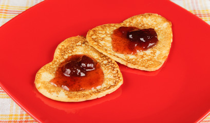 Two pancake in the shape of a heart on a red plate with strawberry jam