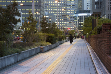 都会の夕暮れの歩道を歩くビジネスマン