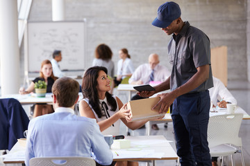 Courier Collecting Package From Businesswoman In Busy Office