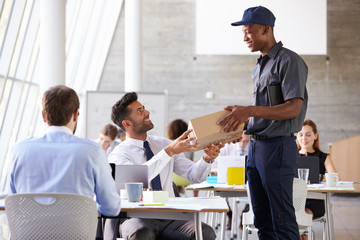 Courier Collecting Package From Businessman In Busy Office