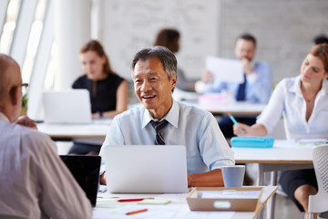 Businessman Working On Laptop In Busy Office