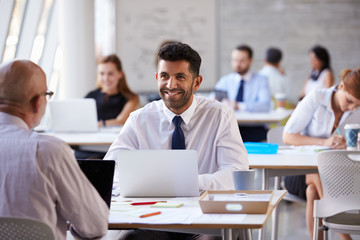 Businessman Working On Laptop In Busy Office