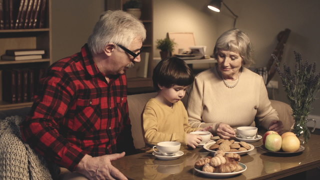 Loving grandparents treating their cute little grandson with tea and pastry