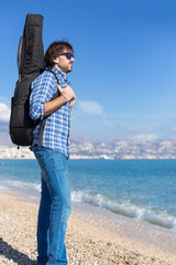 Side view of bearded man with guitar in backpack on coastline