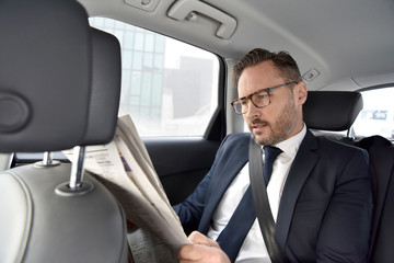 Businessman in taxi cab reading newspaper