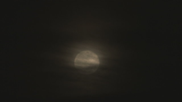 Still shot of a full moon with clouds in front
