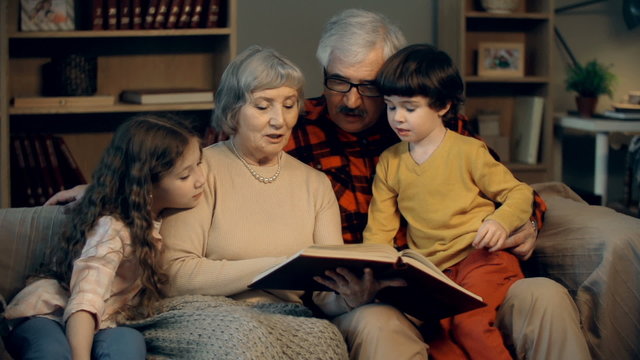 Grandparents and grandchildren reading a book together in the evening 