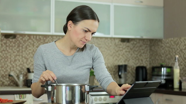 Brunette woman in kitchen following recipe on digital tablet