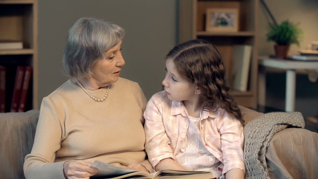 Grandmother reading a book to her granddaughter and discussing a story with her 