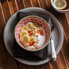Natural yoghurt with banana, dried apricots and crunchy granola in a vintage bowl on a dark wooden table