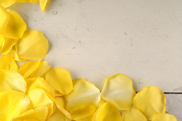 Frame of yellow rose petals on a wood background.
