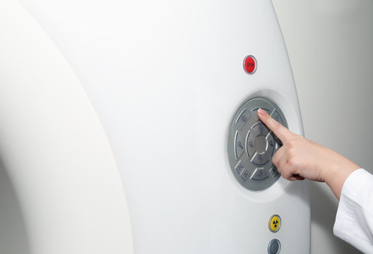 A female doctor's hand pushing control button on CT scanner