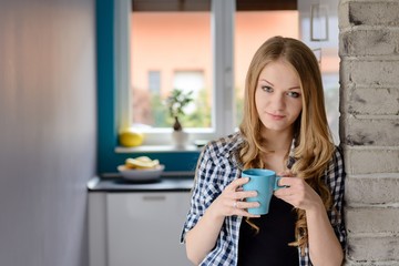 Beautiful blue-eyed blond woman drinking coffe or tea from the cup.