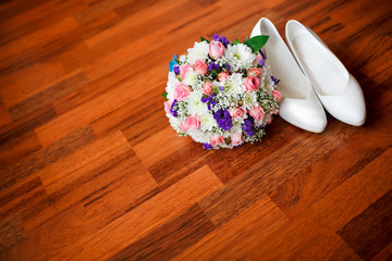 Wedding bouquet with violet flowers and white bride's wedding shoes on the parquet floor, room for copy. Bridal accessories.