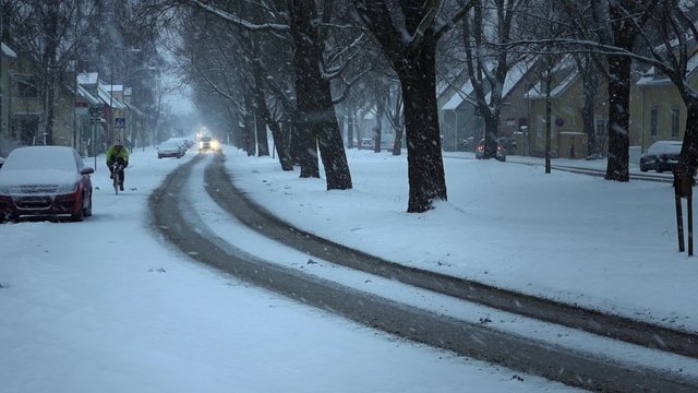Heavy snowfall on street in old suburb with villas. Cars driving slowly. Man on bicycle passing by.