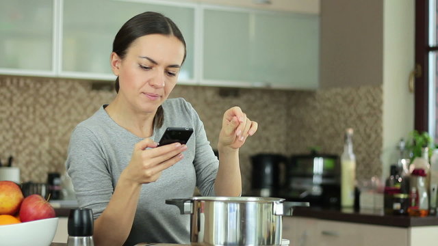 Brunette Woman In Kitchen Following Recipe On Mobile Phone