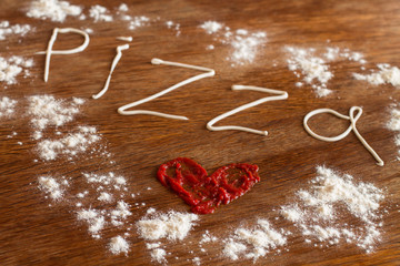 Painted heart of ketchup, written text "pizza" of mayonnaise and flour on wood table.