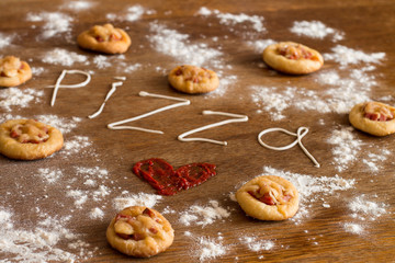Mini pizzas with sausage and cheese on wood table.  Painted heart of ketchup, written text 