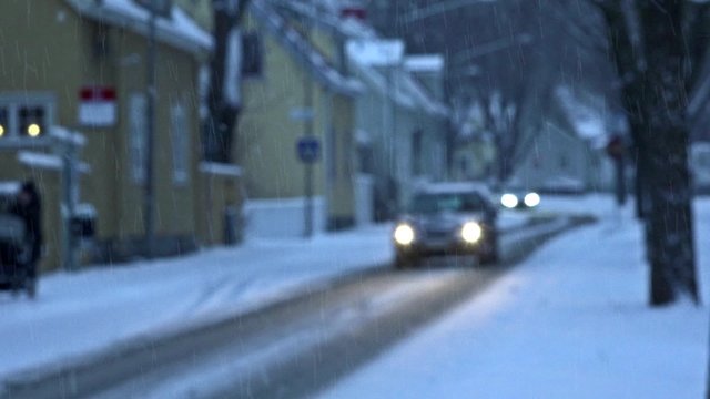 Heavy snowfall on street in old suburb with villas. Cars driving slowly. Focus on snowflakes.

