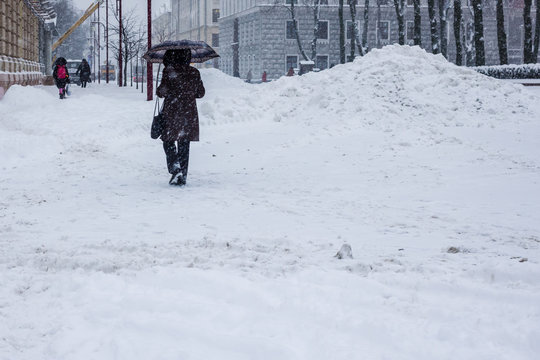 Snow storm in a city, pile of snow and a woman with umbrella