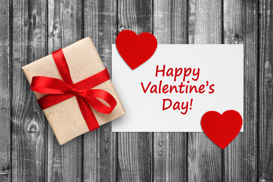Valentines card with gift box and red hearts on black and white wooden background