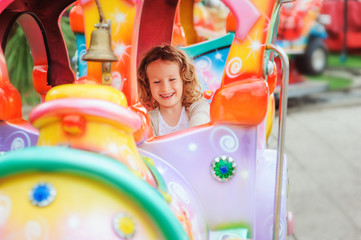 happy child girl riding train on funfair on summer vacation