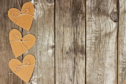 Side border of rustic heart shaped cardboard gift tags against a vintage wood background