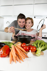 American couple at home kitchen smiling happy together wife cooking husband tasting the vegetable stew