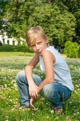 Fototapeta premium Boy sits on his haunches in the park on the green grass