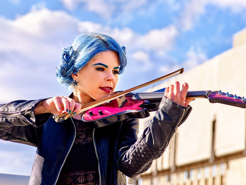 Beautiful music street performers girl violinist with blue hair playing  aganist sky with clouds outdoor.