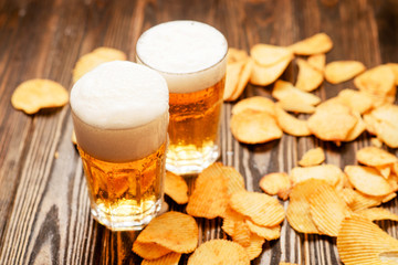 Light foamy beer with potato chips on a wooden background