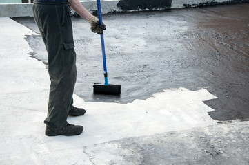 Roofer worker painting  bitumen praimer at concrete surface . Waterproofing. Waterproof roof.