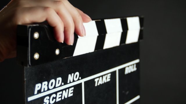Hands holding a film clapper board, on black, close up