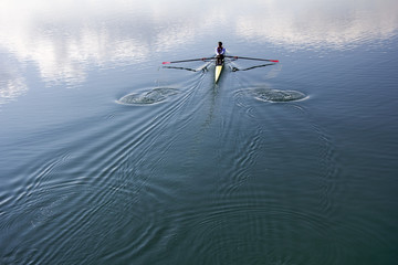 Young man in a boat, rowing on the tranquil lake