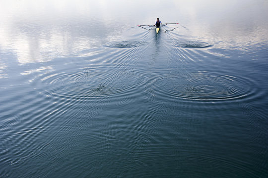 Young man in a boat, rowing on the tranquil lake
