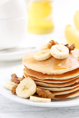 Tasty pancakes with banana and walnut on white wooden background