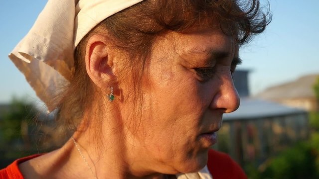 Woman aged in shawl smoking a cigarette in slowmotion at outdoors in summer time