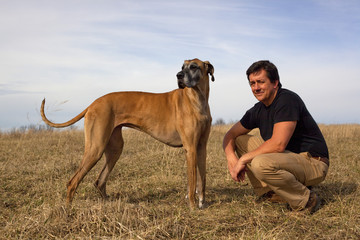 Handsome man crouching in hay field with his great Dane looking left