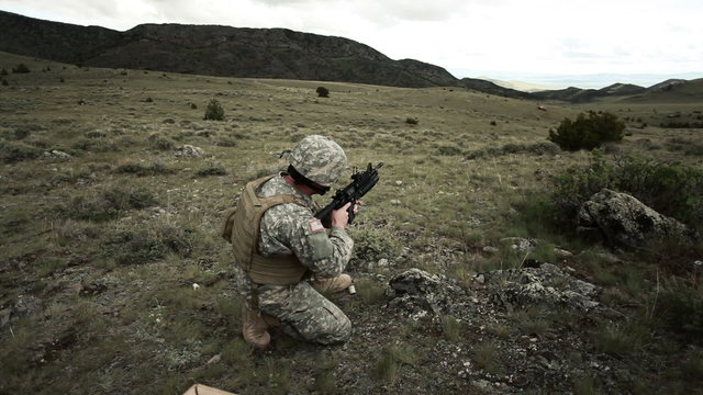 Soldier firing 40 mm grenade launcher attached to M4 assault rifle while kneeling.