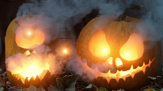 Video for Halloween. Two terrible pumpkins against dry leaves and an oil lamp with smoke in the evening