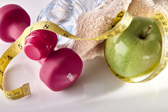 Apple dumbbells and tape measure on white table elevated top